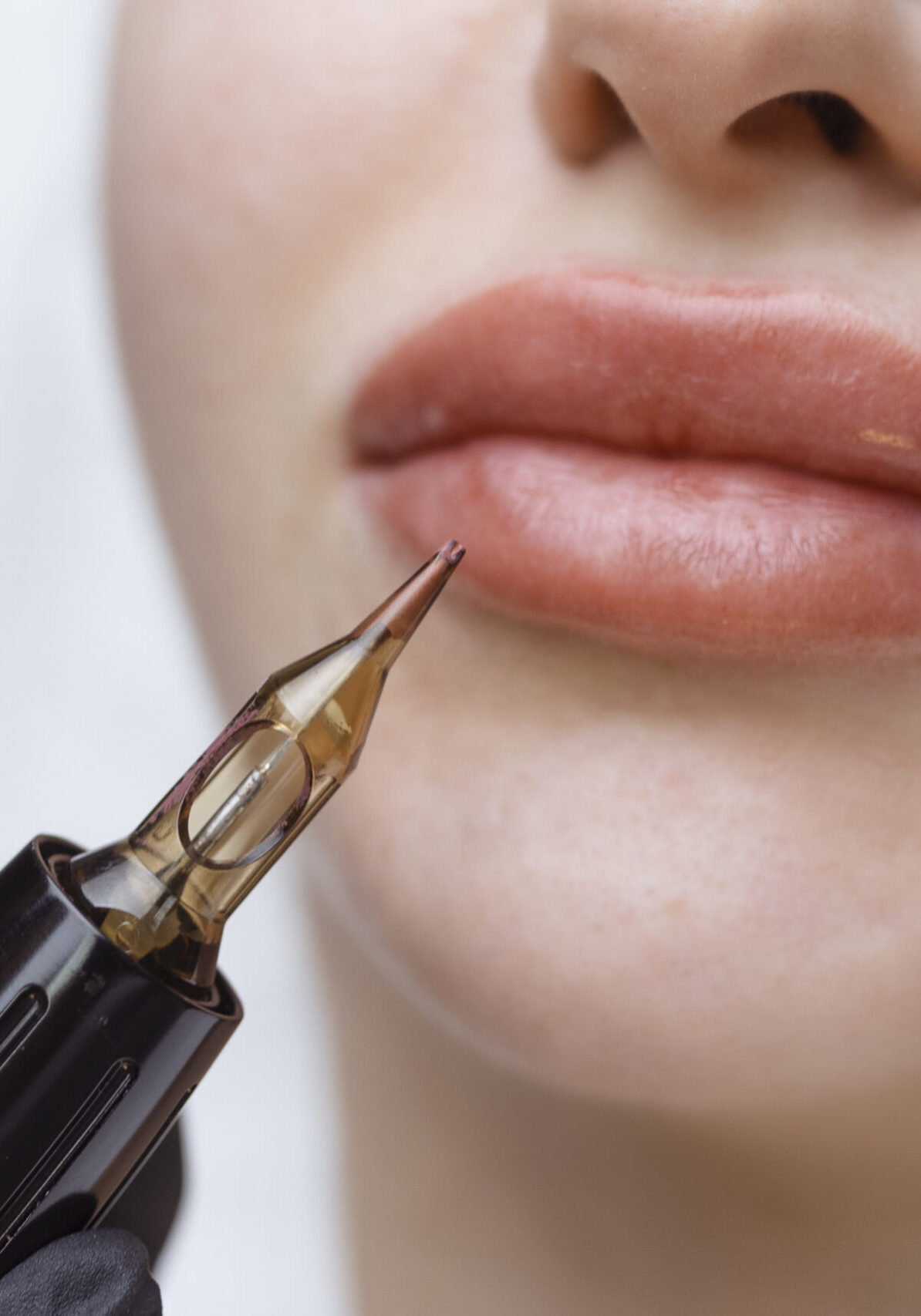 Cosmetologist makes permanent makeup on a woman's face. Specialist applies a tattoo on the patient's lips close-up.
